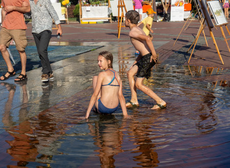 Batumi, Georgia. 08.19.2023  Children play in the fountain. Children's games in the city. Salvation from the heat in the water. Childhood concept. Lots of water splashes. Wet clothes on a man. in a puddleのeditorial素材