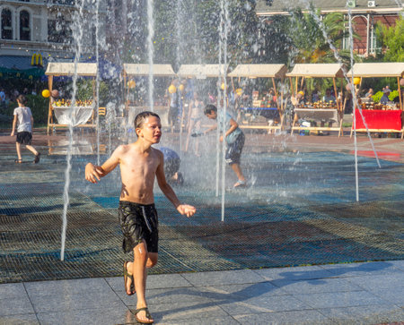Batumi, Georgia. 08.19.2023  Children play in the fountain. Children's games in the city. Salvation from the heat in the water. Childhood concept. Lots of water splashes. Wet clothes on a man.のeditorial素材