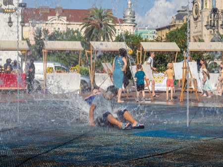 Batumi, Georgia. 08.19.2023  Children play in the fountain. Children's games in the city. Salvation from the heat in the water. Childhood concept. Lots of water splashes. Wet clothes on a man.のeditorial素材