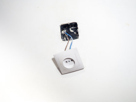Broken electrical socket on the wall. Disassembled device. White wall with a socket pulled out of the wall. Life threatening. Broken electrical equipment concept. Appliances. Wires out. Lifeの写真素材