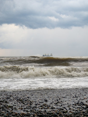 lonely ship in the middle of a rough sea. Barge in the distance. Big waves on the sea. After the storm. Bad weather. Danger. Ship on the horizonの写真素材