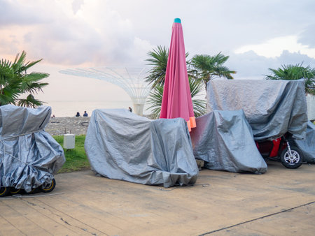 Vehicles at the resort are covered with tarps. Bicycles and scooters at the resort. The concept of the end of the holiday season. Rain protection. Business of entertainment on vacationの写真素材