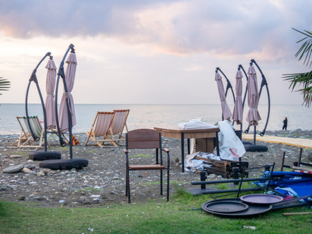 outdoor restaurant at the resort is closing its doors. Dismantling furniture and umbrellas in a cafe. Dismantling a cafe at sea. Business winding down. The concept of the end of the holiday season. Approaching storm. Resort in autumn. Business on vacationの写真素材