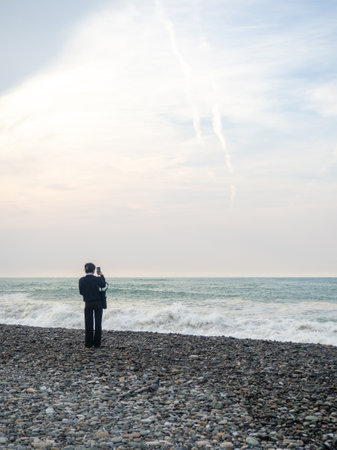 Lonely woman on the seashore. Looks at the waves. Walks along the coast. Off-season at the resort. Autumn in the south. Subtropics in the coldの写真素材