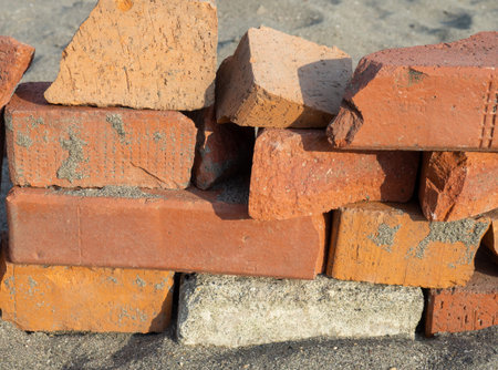 Old red bricks stacked on the sand. Broken bricks. Building materials unsuitable for use