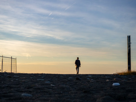 A man in headphones walks along the shore to the sea. A man goes to watch the sunset. A resort place. Solitude. Silhouette of a guyの写真素材