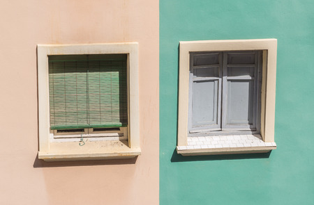 two windows with colorful facade of a residential building shutters and wooden windows orange and green pastelの写真素材