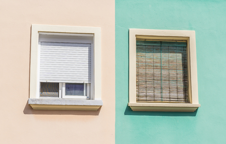 two windows with colorful facade of a residential building wooden shutters orange and green pastelの写真素材