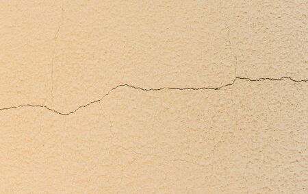 thin horizontal crack in a light yellow concrete wall texture backgroundの写真素材