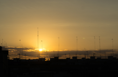 Silhouettes of buildings in at sunset at the city skyline with antennas and cablesの写真素材