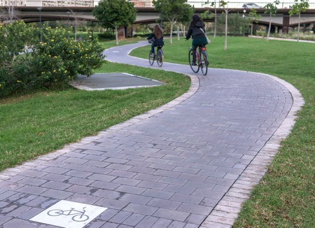 cycleway signposted a ground bikeway with two cyclists circling. Bike lane between trees in Jardin del Turia in Valencia Spainの写真素材