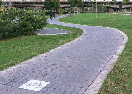 cycleway signposted a ground bikeway with two cyclists circling at background. Bike lane between trees in Jardin del Turia in Valencia Spainの写真素材