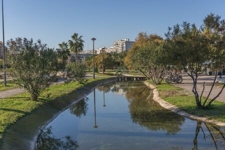 Gardens in the old dry riverbed of the Turia river - reflection of trees in the artificial water channel and small bridge in the background. Valencia, Spain,の写真素材