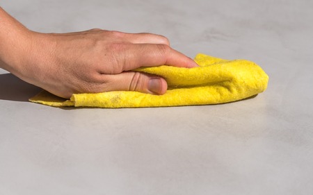 womans hand cleaning spilled water on a cement floor with a yellow floor cloth dishcloth closeupの写真素材