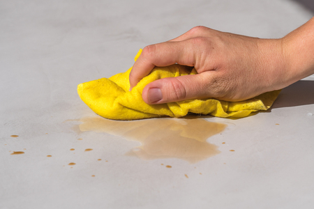 womans hand cleaning tea stain or spilled coffee on a cement floor with a yellow floor cloth dishcloth closeupの写真素材