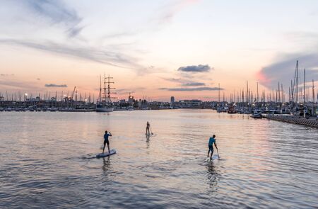 Silhouette of stand up paddle boarder paddling at sunset on a flat warm quiet seaの写真素材
