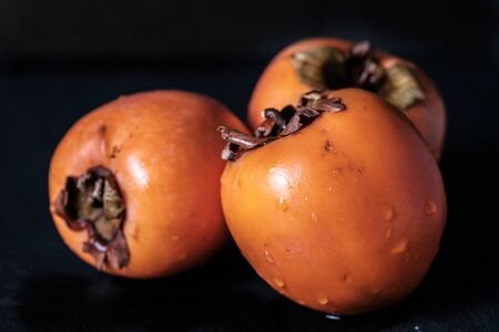 Three persimmon Kaki fresh and wet isolated on black background wholeの写真素材