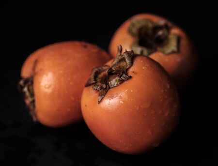 Three persimmon Kaki fresh and wet isolated on black background wholeの写真素材