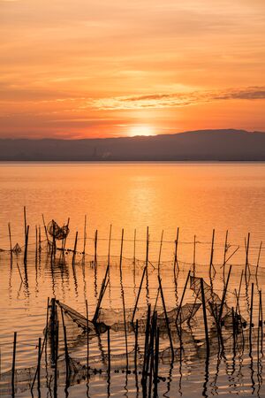 Sunset pier Albufera Valencia reflections orange sky in the lake Naural Park Spain. traditional fishing nets in the waterの写真素材
