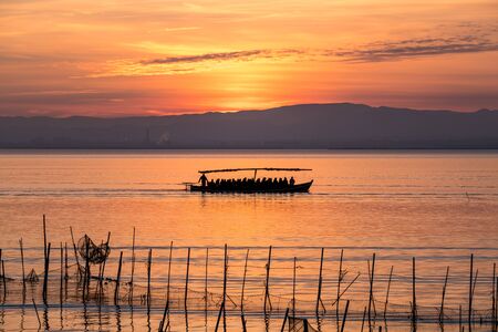 Sunset pier Albufera Valencia tourist ride boat reflections orange sky in the lake Naural Park Spain. traditional fishing nets in the waterの写真素材