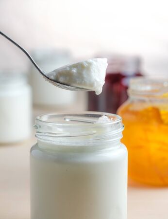 Homemade yogurt with orange marmalade spoon eating from a glass jar on a white wooden table. Healthy dairy probiotic breakfast.の写真素材