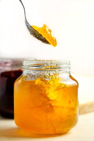 homemade orange marmalade spoon eating jam from a glass jar sweet breakfast over light wooden backgroundの写真素材