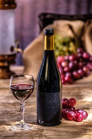 Ripe grapes red wine glass and bottle of wine on a wooden backgroundの写真素材