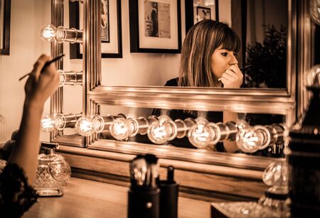 woman looking into a vintage mirror at herself and use cosmetic vanity make up accessories, makeup dressing tableの写真素材