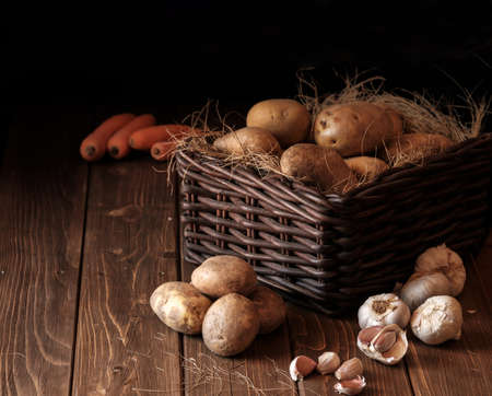 potatoes garlic carrot vegetable still life raw food wicker basket rustic wooden floorの写真素材