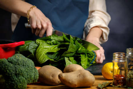 A woman is cutting spinach on a kitchen boardの写真素材