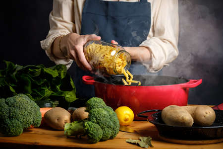 A woman cooking boils pasta in a saucepan with steamの写真素材