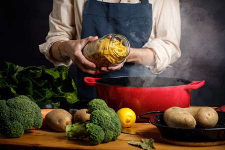 A woman cooking boils pasta in a saucepan with steamの写真素材