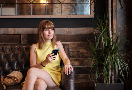 woman using her mobile phone on the sofa an elegant cafe interior, staring into space thinkingの写真素材