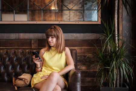 woman using her mobile phone on the sofa an elegant cafe interiorの写真素材