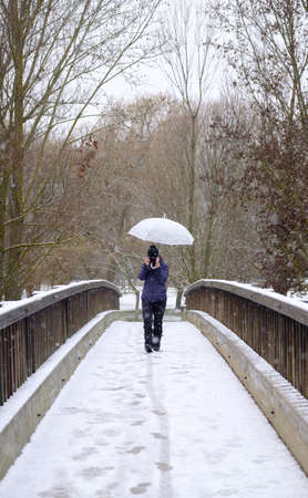 Candamia park snowy day in winter girl walking across a wooden bridge with her photo camera and holding an umbrella, Leon Spainの写真素材