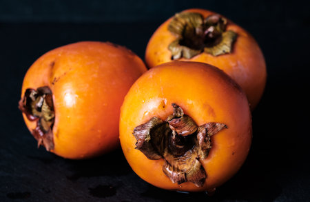 persimmon Kaki fresh and wet isolated on black background chiaroscuro mysterious atmosphereの写真素材