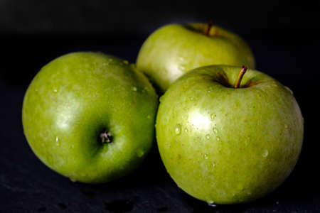 Green apple, fresh and wet fruit isolated on black background gloomy chiaroscuro mysterious atmosphereの写真素材
