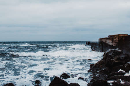 Stormy seascape on a cloudy day. Sea waves crash against the rocks.の写真素材