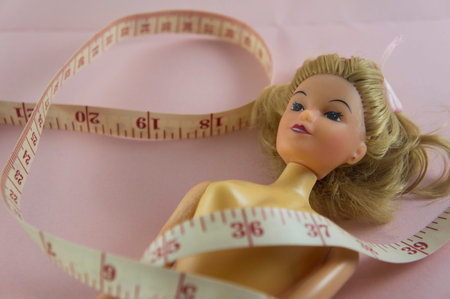closeup measuring tape with women plastic doll on pink background