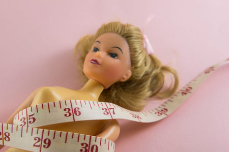 closeup measuring tape with women plastic doll on pink background