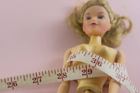 closeup measuring tape with women plastic doll on pink backgroundの写真素材