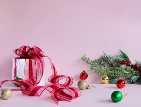 In the picture include: Gift box and Red bow, Pine tree branch, and many Colored balls in Pink background .の写真素材