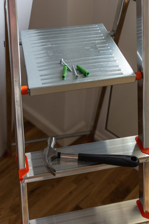 Hammer with screws and wall plugs on the stepladder, repairs in the house