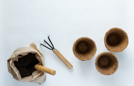 Rakes and eco friendly pots for seedlings on a white background, small bag with ground and garden trowelの写真素材