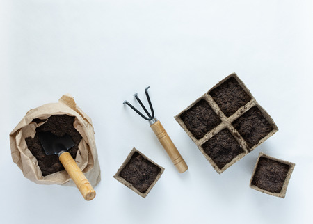 Eco friendly pots for seedlings and rakes on white background, small bag with ground and garden trowelの写真素材