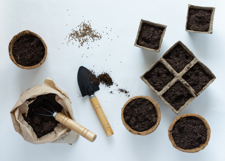 Eco friendly pots for seedlings and seeds on white background, small bag with ground and garden trowel and rakesの写真素材