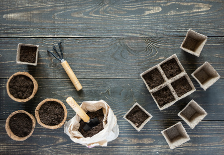 Rakes and eco friendly pots for seedlings on wooden background, small bag with ground and garden trowel and rakesの写真素材