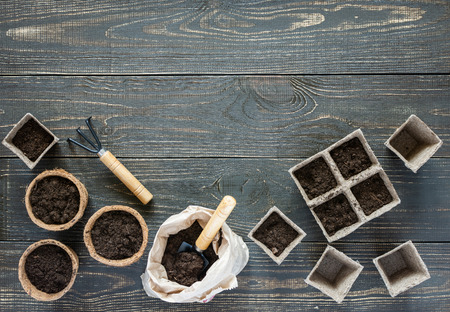 Rakes and eco friendly pots for seedlings on wooden background, small bag with ground and garden trowel and rakesの写真素材