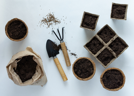 Eco friendly pots for seedlings and seeds on white background, small bag with ground and garden trowel and rakesの写真素材