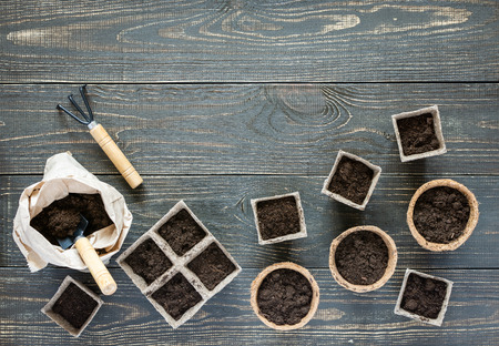 Rakes and eco friendly pots for seedlings on wooden background, small bag with ground and garden trowel and rakesの写真素材